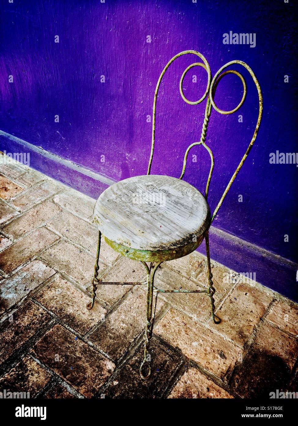 Una sedia rustica contro un viola parete dipinta aggiunge fascino e carattere. Foto Stock