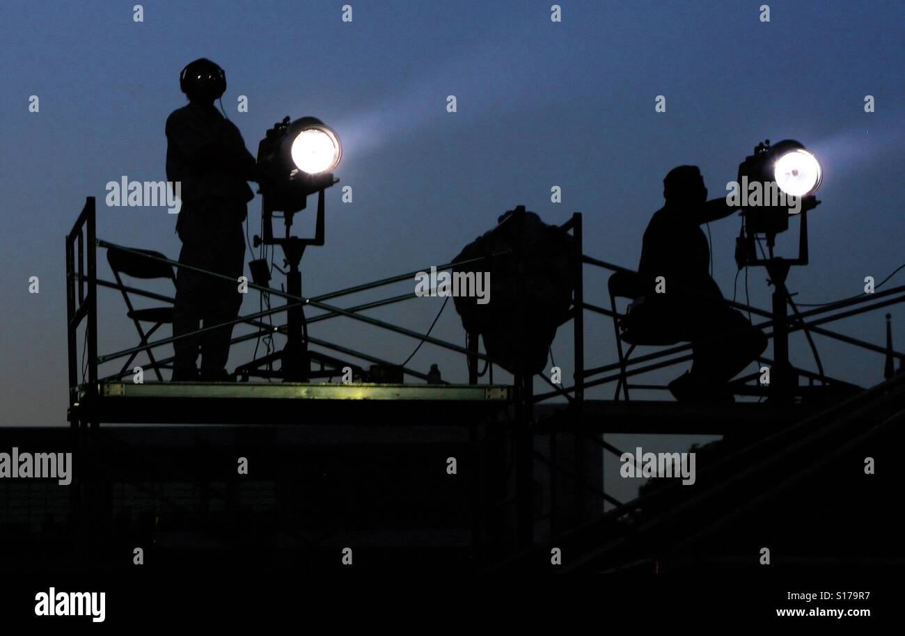 I tecnici di un fulmine su un ponteggio illuminare il palco durante un concerto di musica all'aperto - Immagine stock catturata con smartphone