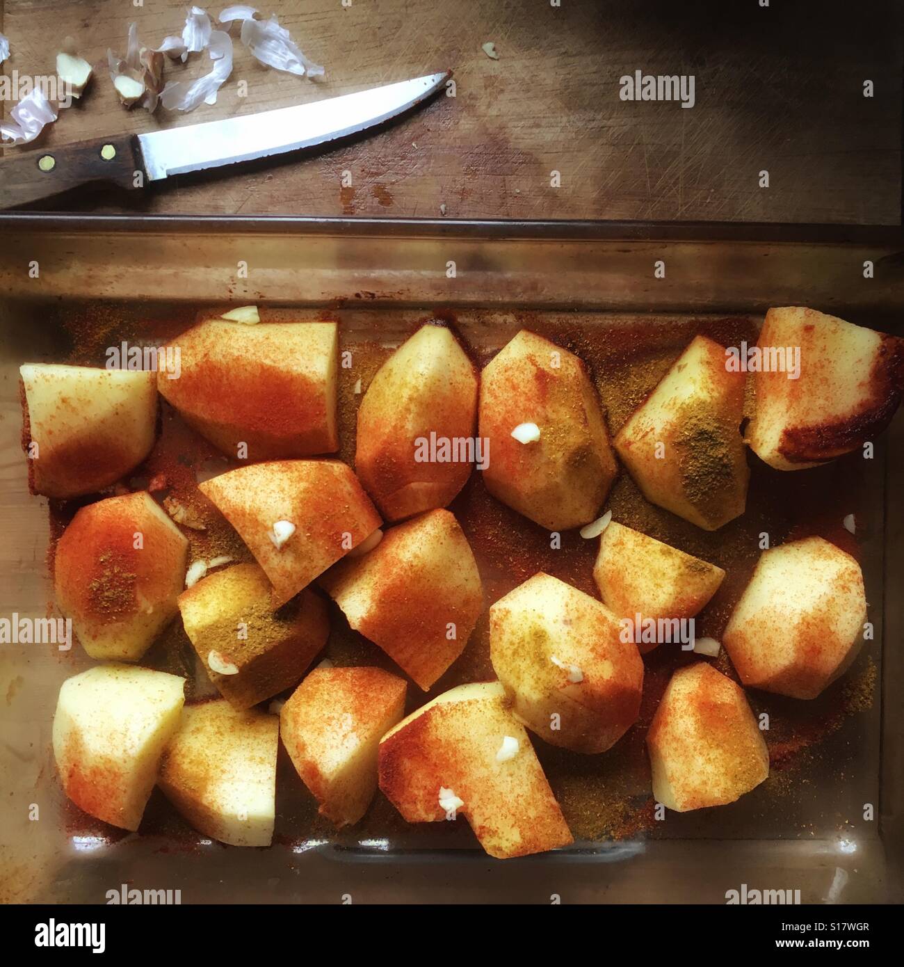 La preparazione di patate arrosto spolverate con paprika curry in polvere e aglio schiacciato Foto Stock