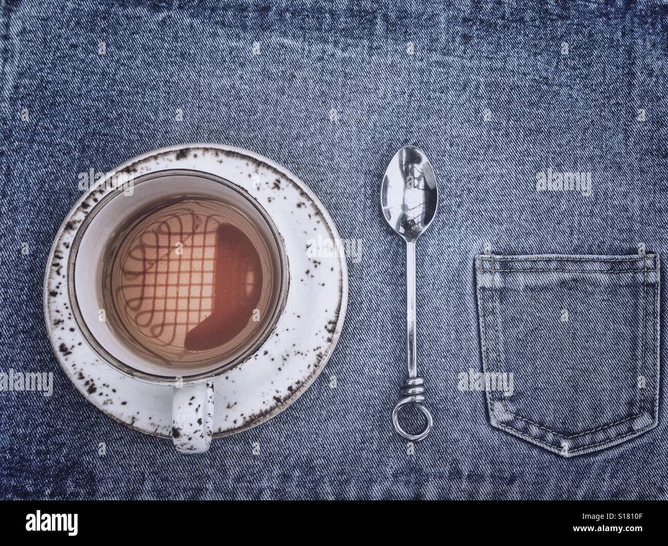 Tazza di tè e un cucchiaio su un paio di jeans tovaglia con una tasca Foto Stock