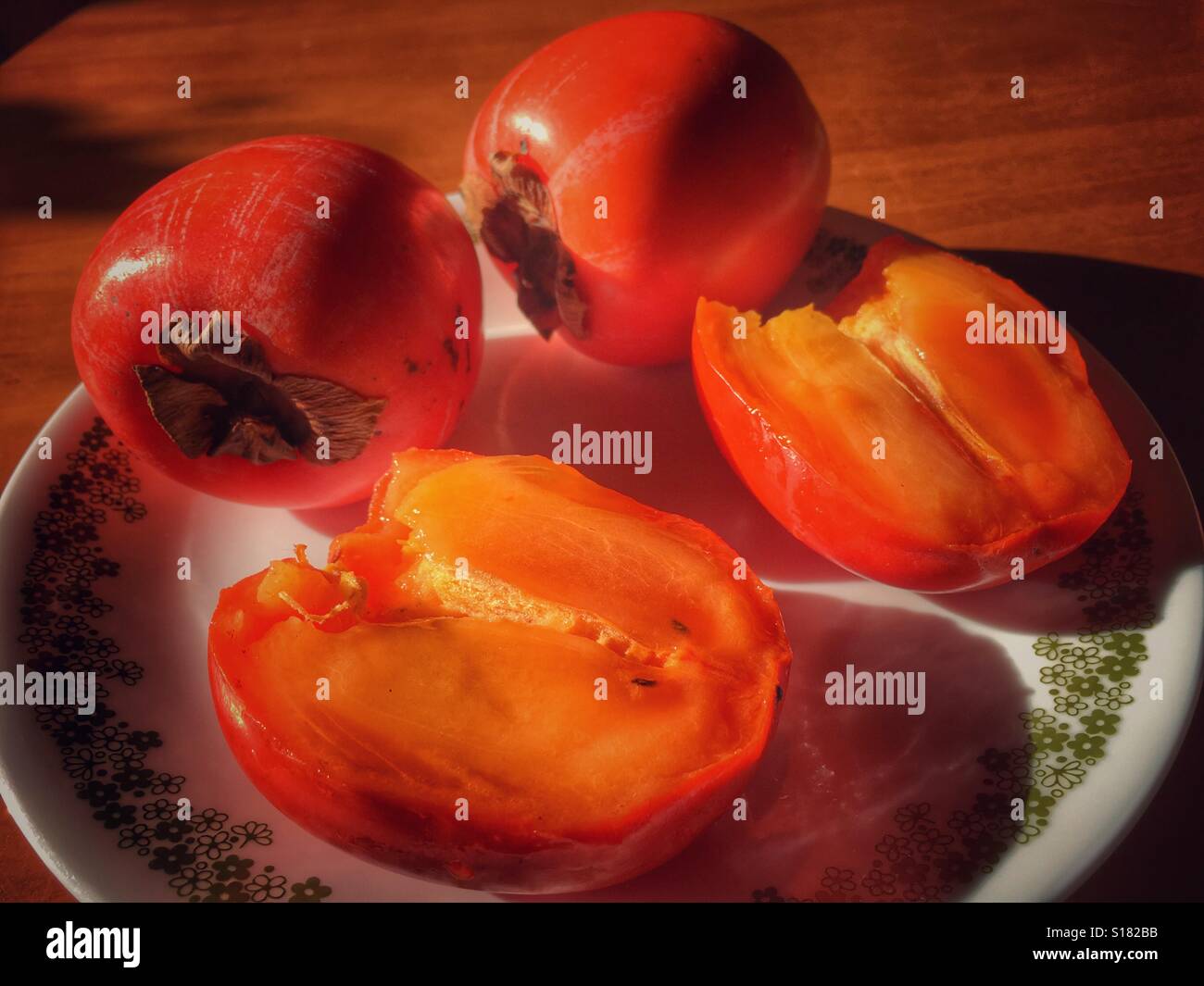 Tre cachi su una piastra, un taglio aperto e pronto a mangiare. - Immagine stock catturata con smartphone