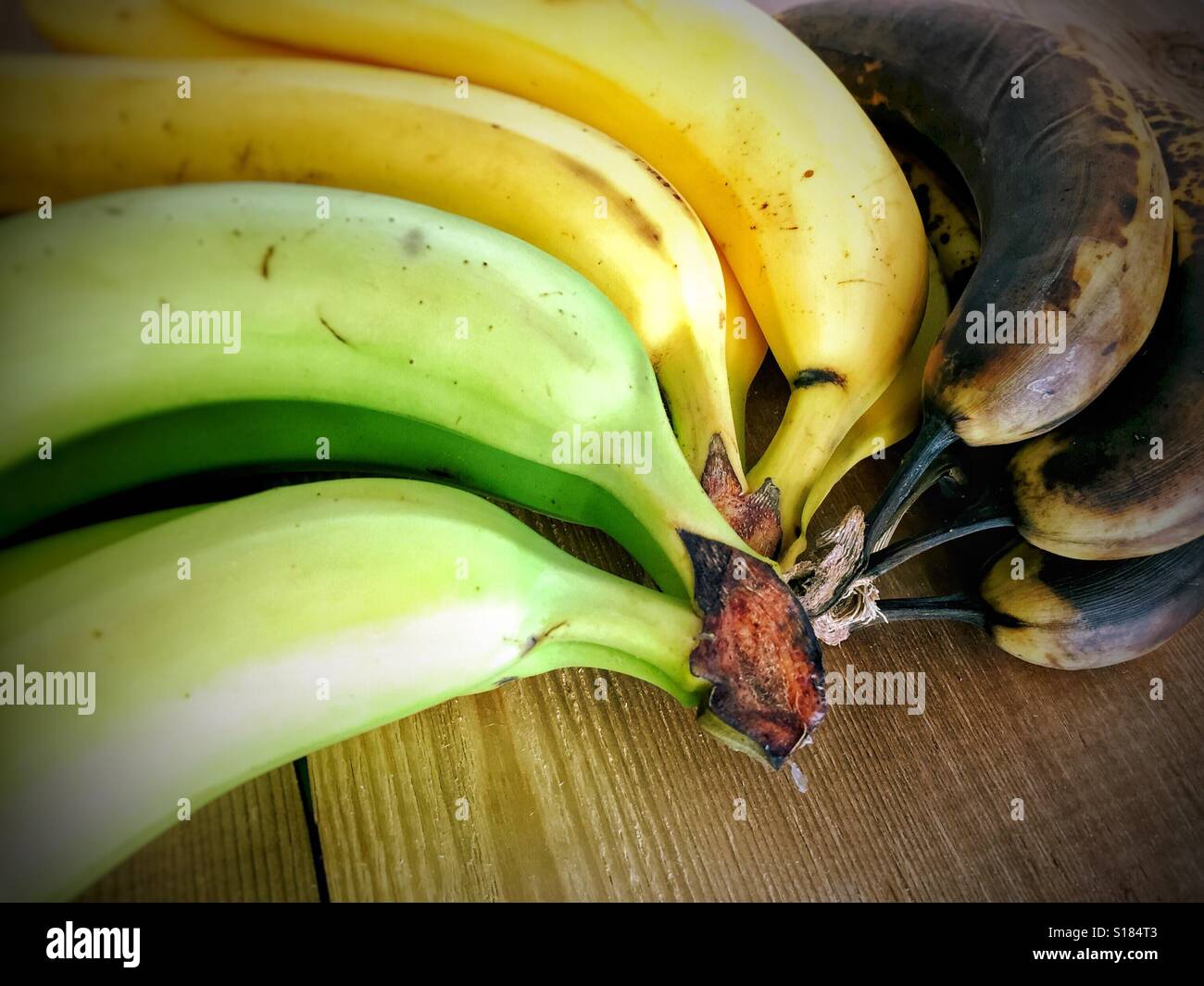 Close up di grappoli di banane a diversi stadi di maturazione su una superficie in legno. - Immagine stock catturata con smartphone