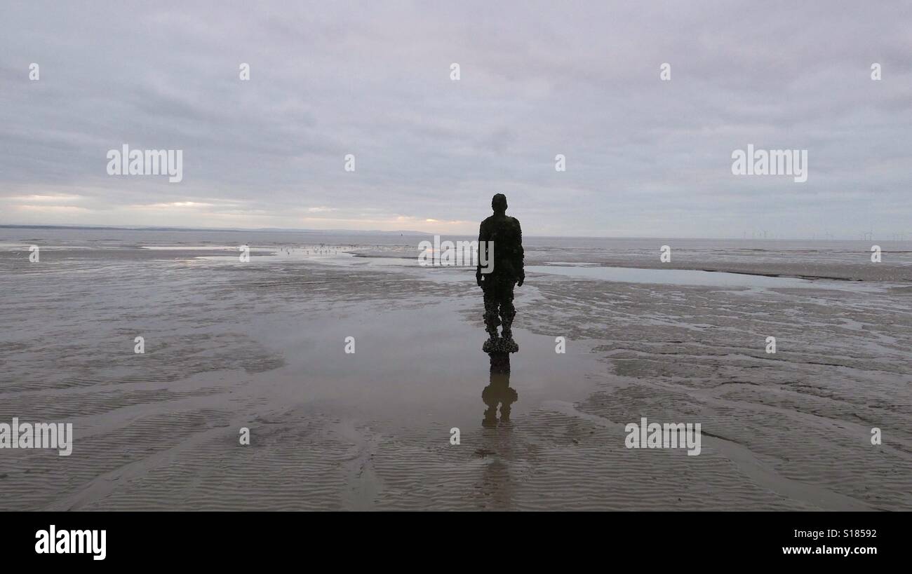 Un altro luogo, Crosby beach. Uno di Antony Gormley di uomini di ferro. Foto Stock