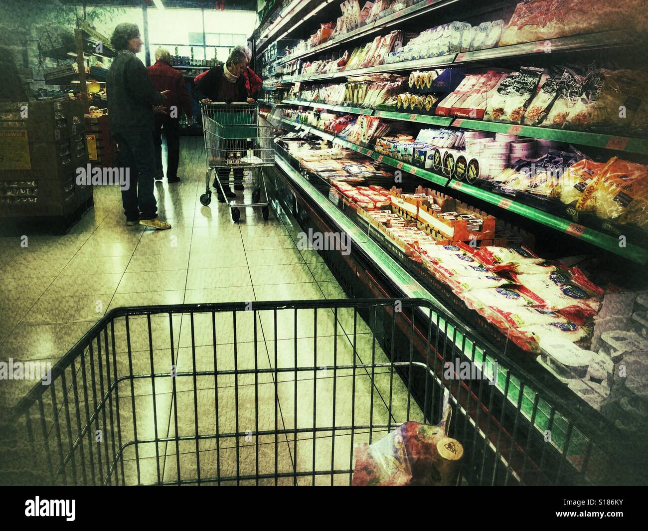 POV spingendo il carrello per supermercati giù il corridoio di formaggio in un supermercato spagnolo - Immagine stock catturata con smartphone