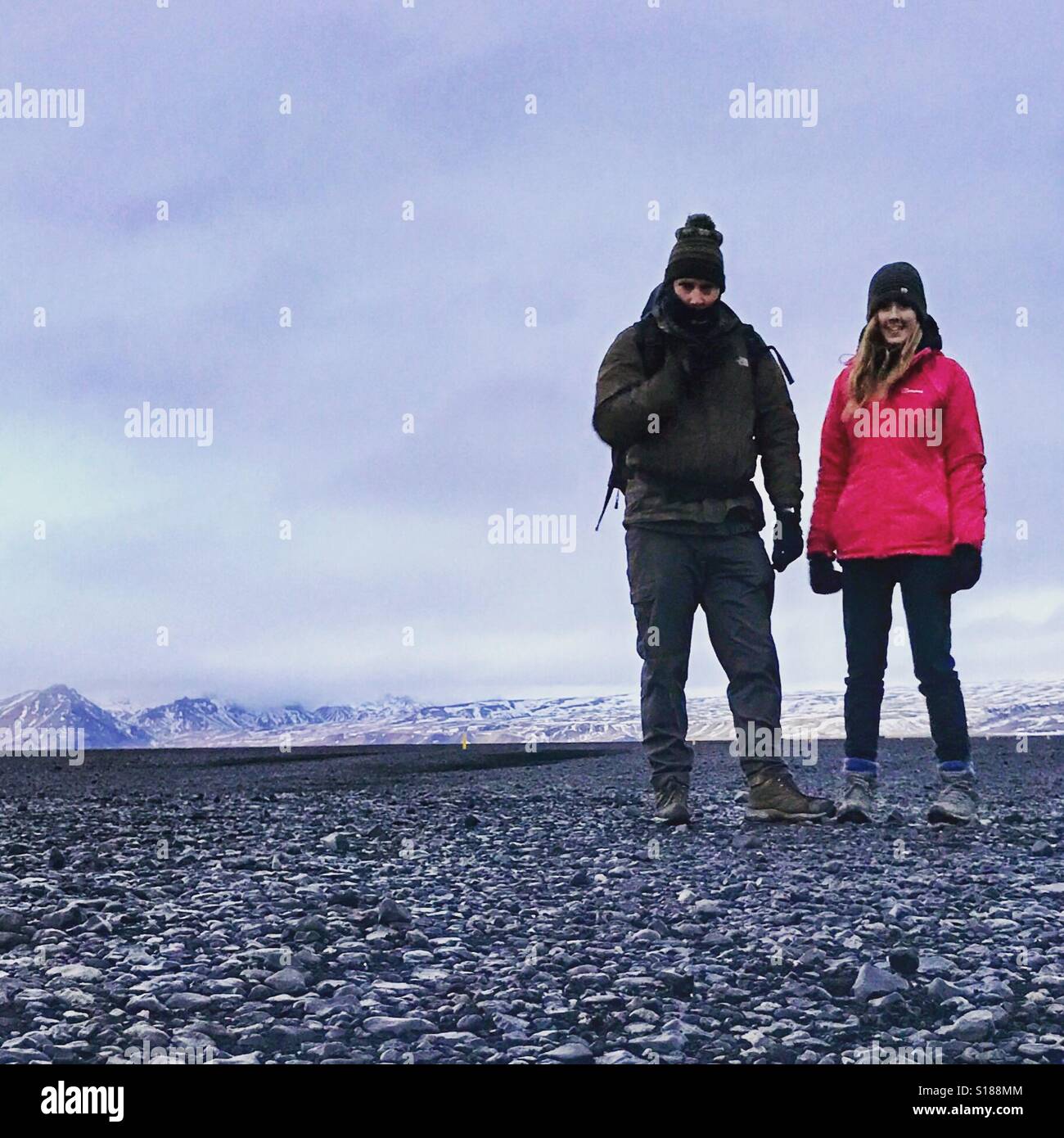 Due persone sulla spiaggia nera in Islanda con montagne coperte di neve in background. Spazio per il testo - Immagine stock catturata con smartphone