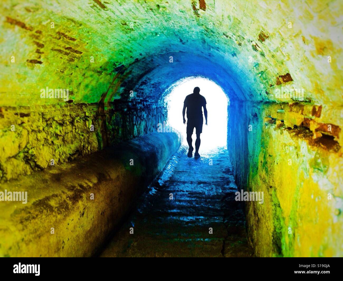 Anonimo silhouette di un uomo a piedi attraverso un sottopassaggio buio che simboleggia la luce alla fine del tunnel - Immagine stock catturata con smartphone