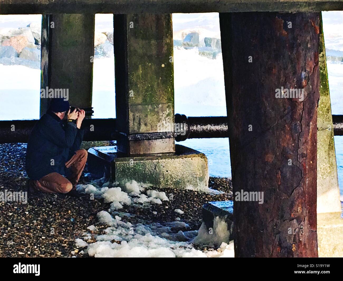 L'uomo prendendo fotografie sotto il molo di Southwold, Norfolk su una giornata invernale Foto Stock