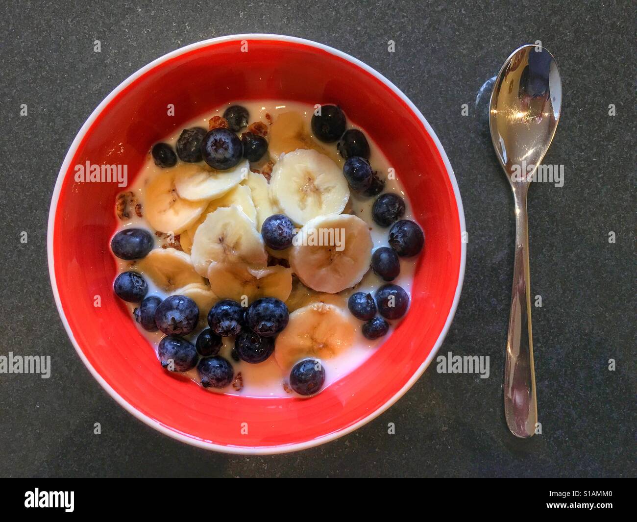 Una sana prima colazione. Ciotola di cereali e latte, guarnita con banane fresche e mirtilli - Immagine stock catturata con smartphone