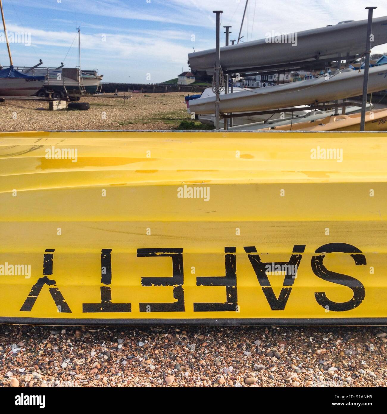 Scritto sicurezza capovolto su una barca di giallo, sicurezza barca su una spiaggia ghiaiosa Foto Stock