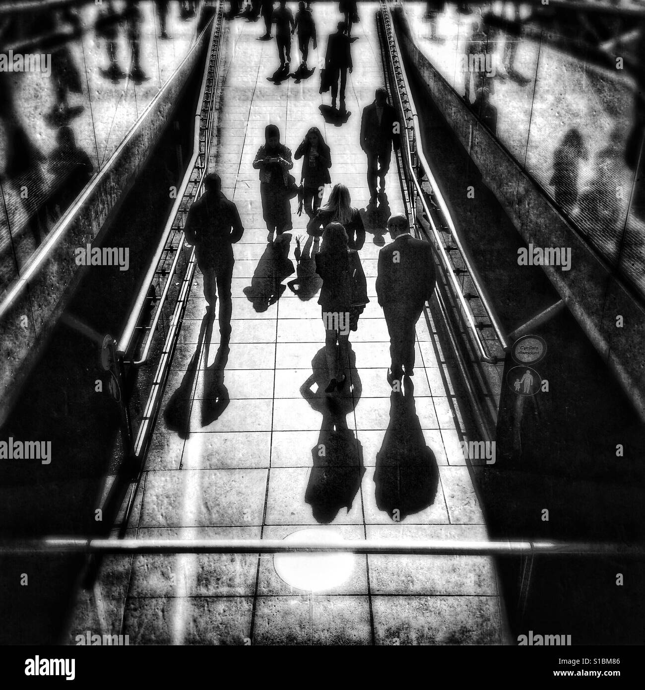 Foto in bianco e nero dei pedoni casting ombre lunghe come essi a piedi dalla base del Millennium Bridge nel sole del pomeriggio, Londra, Inghilterra, Regno Unito. Foto Stock
