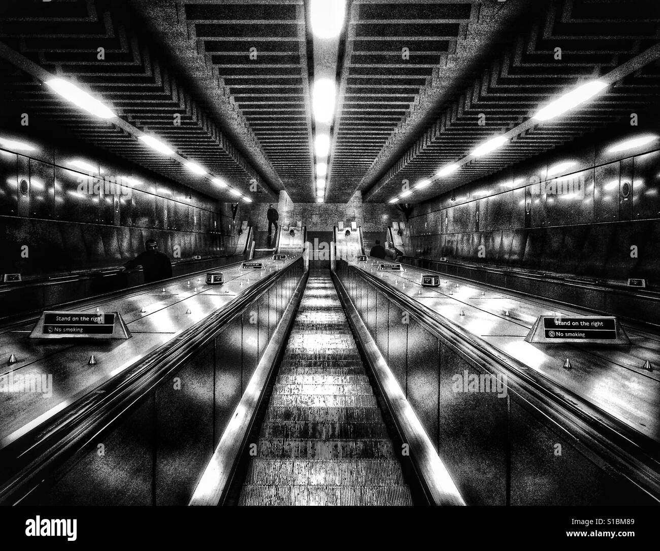 Foto in bianco e nero guardando giù le scale mobili per il loro punto di fuga alla stazione di Tottenham Court Road, Londra, Inghilterra, Regno Unito. Foto Stock