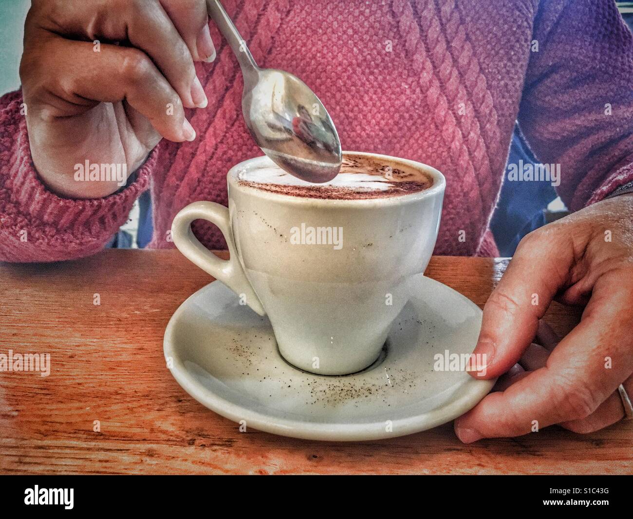 Donna mettendo un cucchiaino in un caffè cappuccino Foto Stock