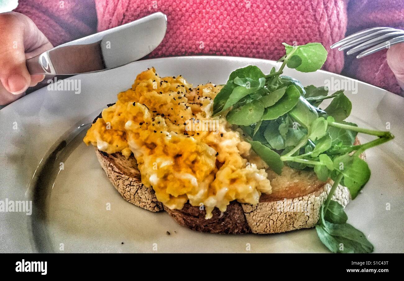 Colazione!!! Uova strapazzate su pane tostato e donna pronto a mangiare con coltello e forchetta in mani. Foto Stock