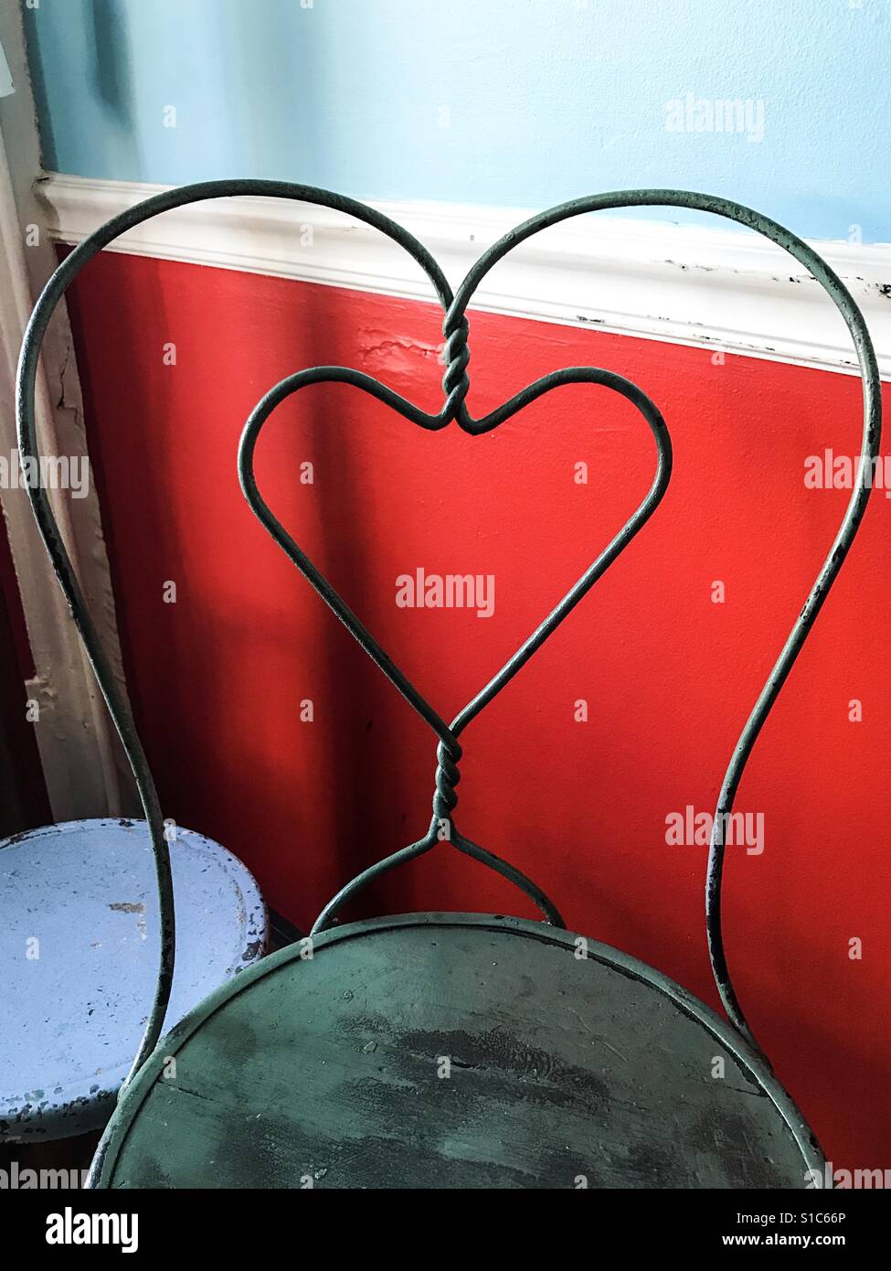 Forma di cuore sul retro di un vuoto sedia in metallo, contro una parete rossa. Foto Stock