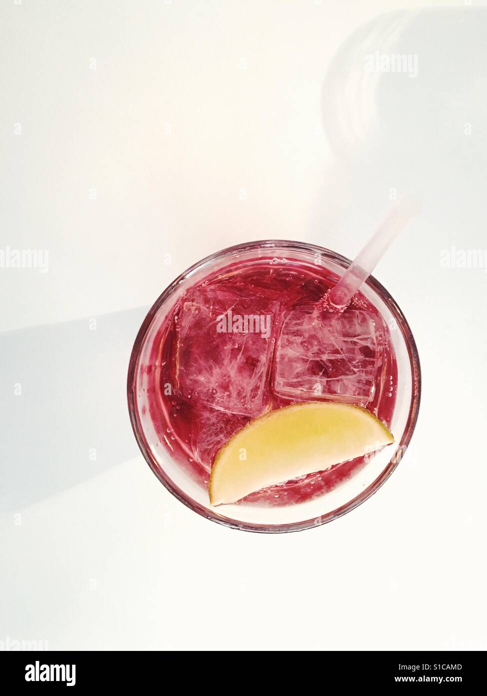 Vista da sopra di una bevanda di colore rosso con anwedge di limone su un tavolo bianco Foto Stock