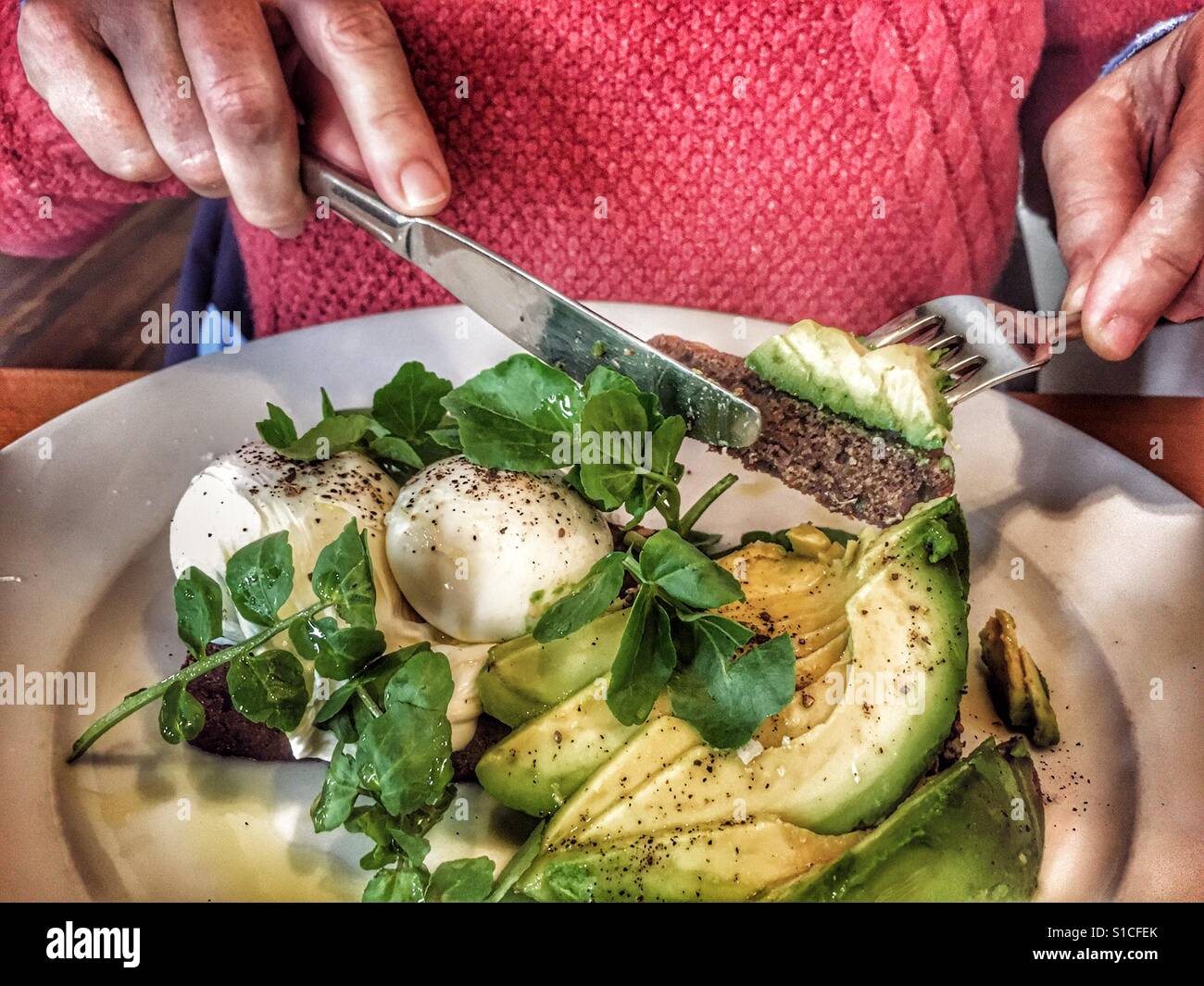 Donna di mangiare uova in camicia su toast con insalata di avocado Foto Stock