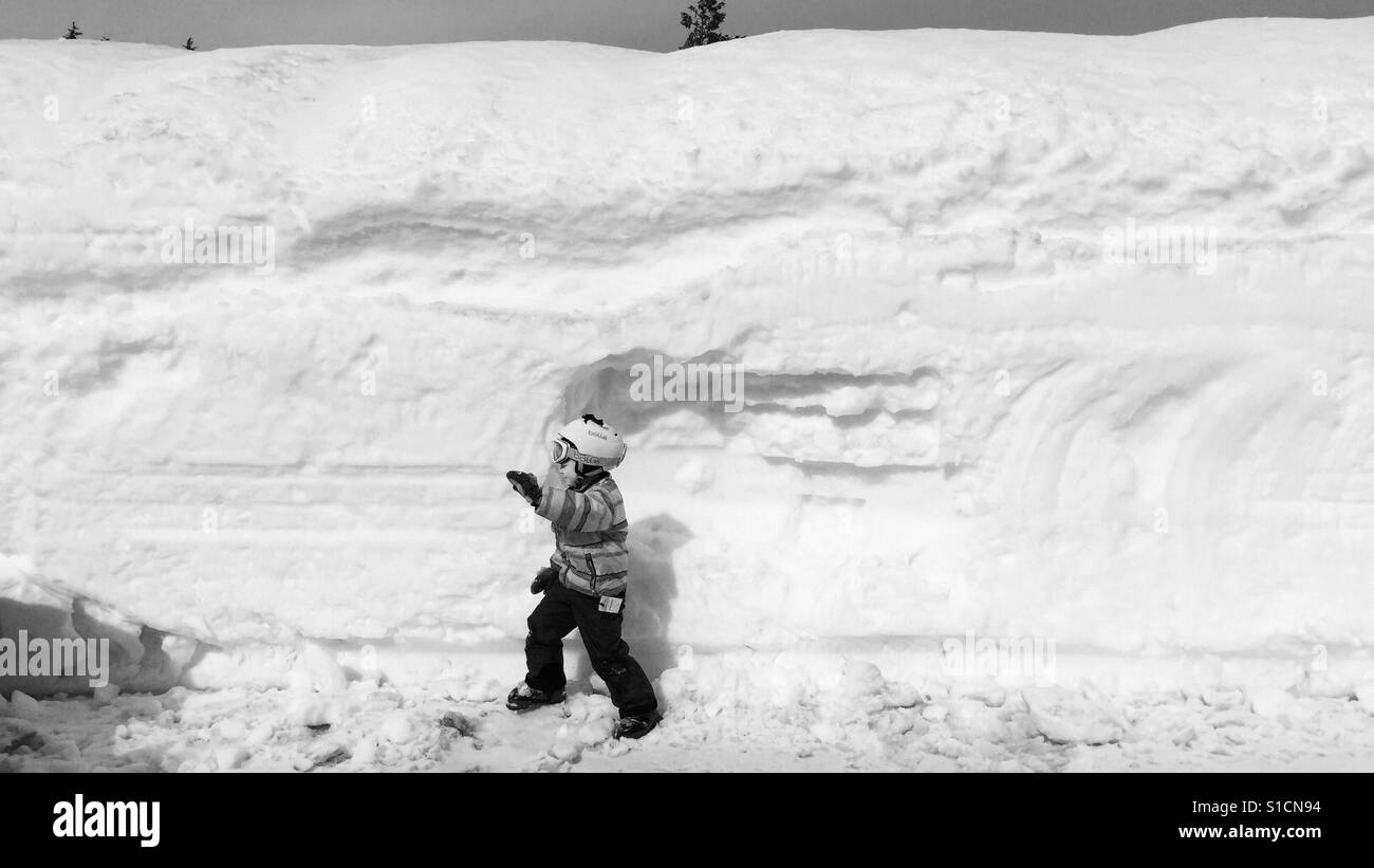Bambino in scarponi da sci a camminare accanto a snow bank Foto Stock