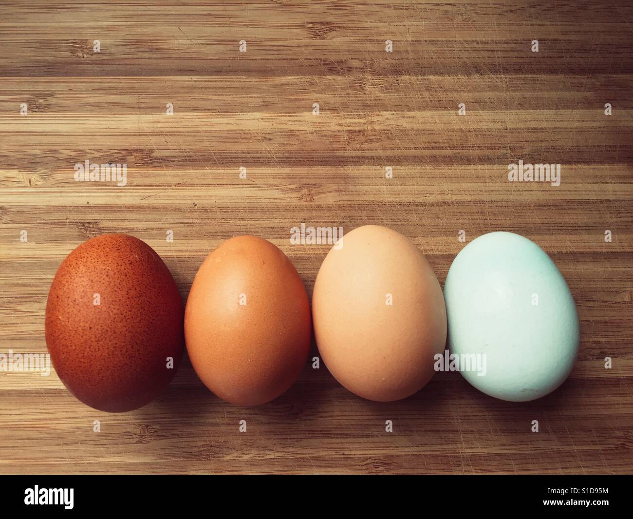 Quattro uova in diverse tonalità di colore su una superficie in legno Foto Stock