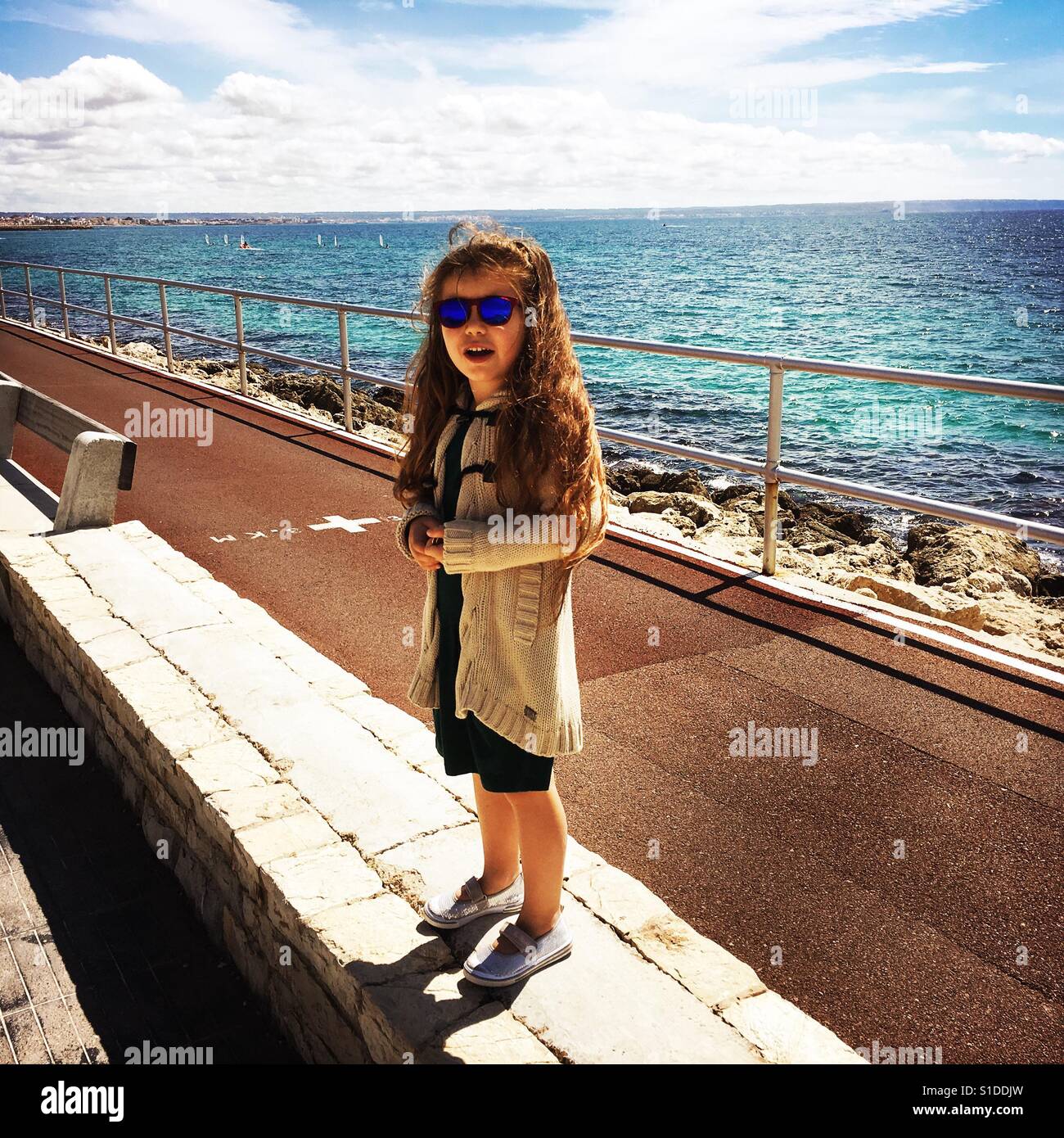 Bambina in piedi su un muro basso torna all'oceano Foto Stock