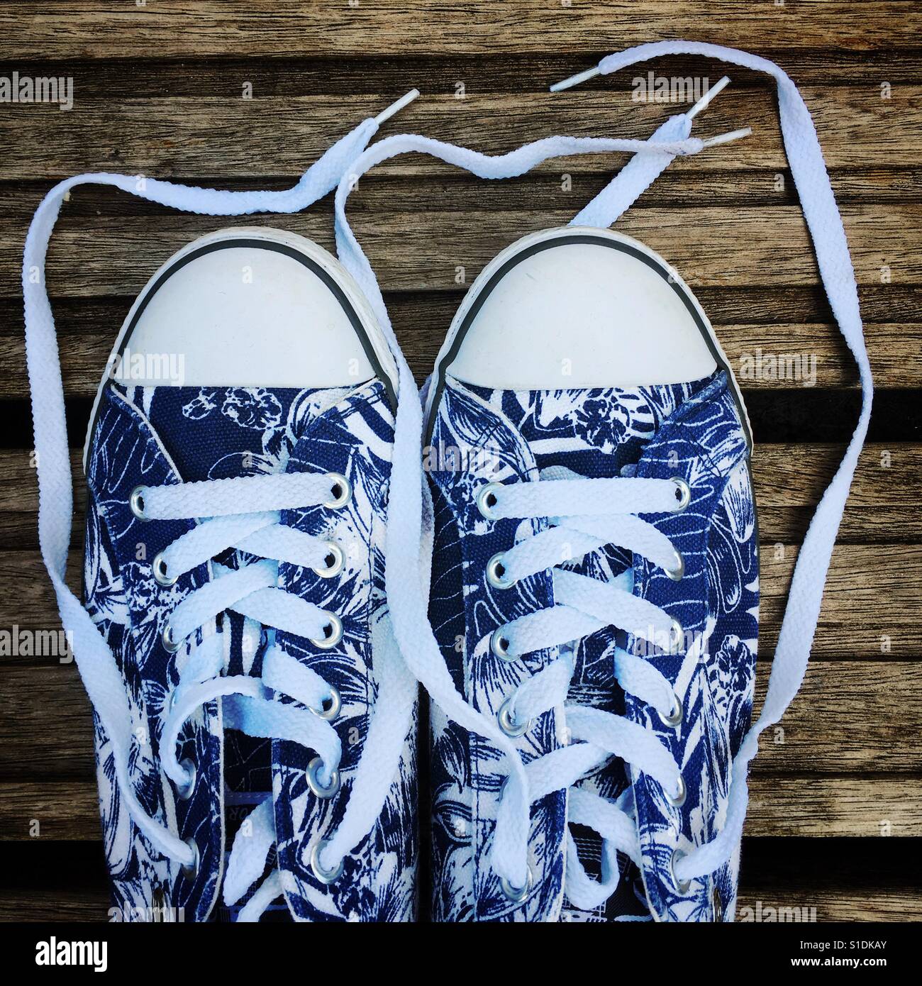 Tela Converse-style formatori con un stile surf blu e bianco fiore pattern print, fotografati contro di legno decking. Foto Stock