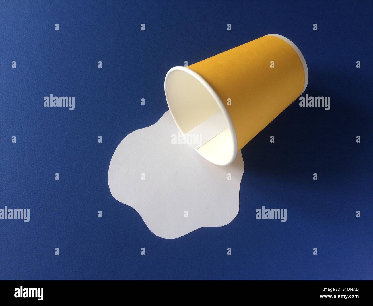 Il latte versato da giallo tazza monouso su sfondo blu. Carta artigianale concetto. Foto Stock