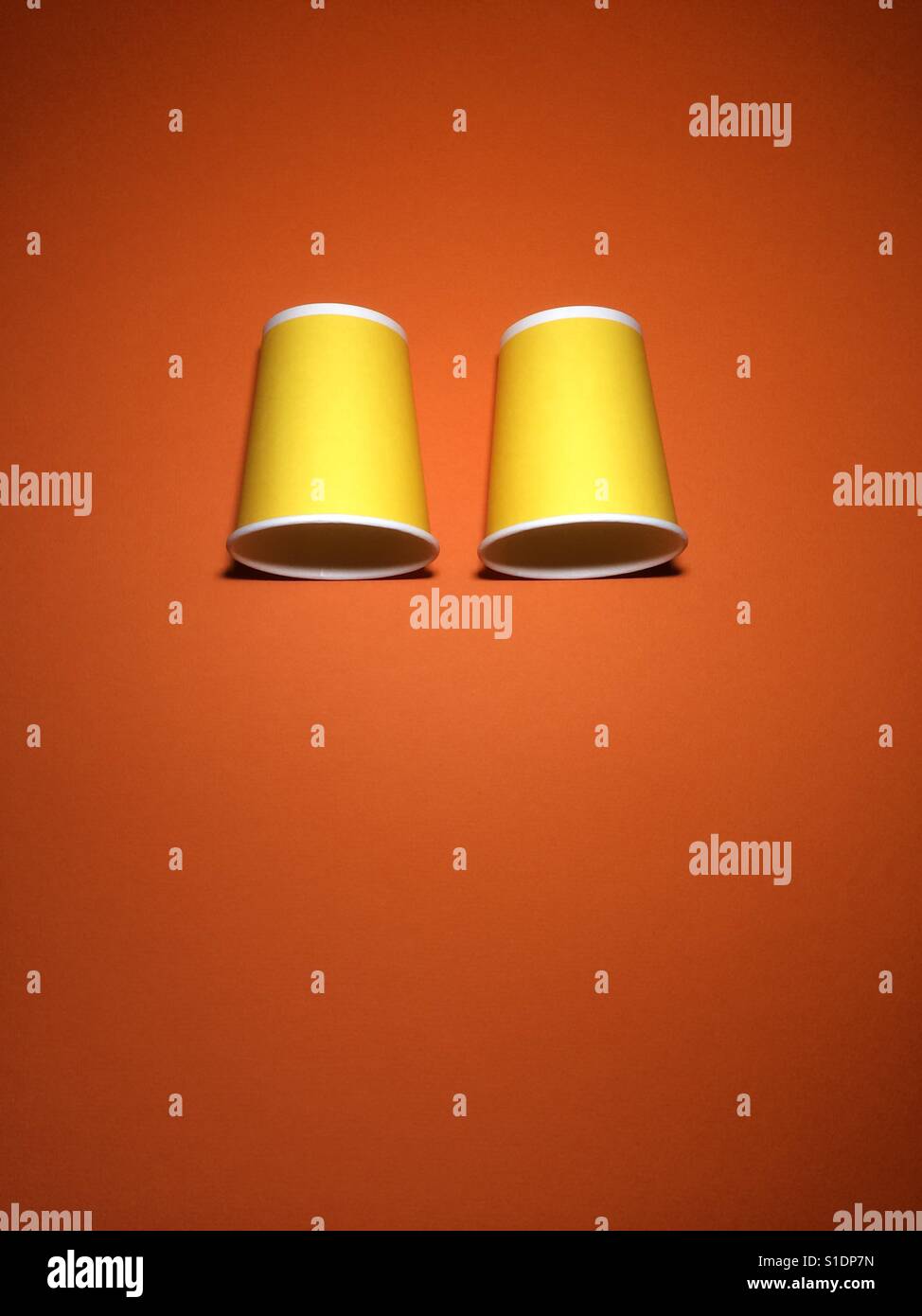 Giallo due tazze monouso su orange carta testurizzata sfondo con copia spazio. Foto Stock