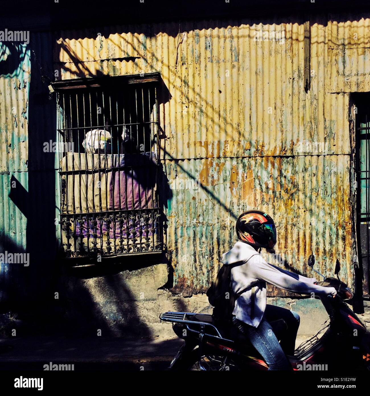 Un uomo di Salvadoran cavalca un motociclo di fronte a una classe bassa house progettata utilizzando l'architettura coloniale spagnola elementi, costruito nel centro di San Salvador El Salvador, 15 novembre 2016. Foto Stock
