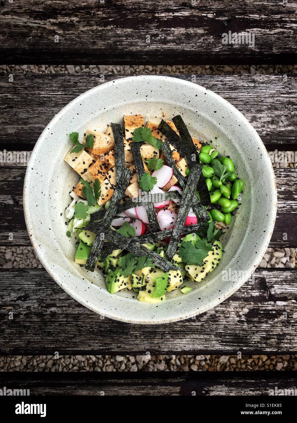 Un bianco ciotola di Hawaiian Poke con tofu, edamame fagioli, avocado, di semi di sesamo nero e strisce di nori alghe su un weathered tavola in legno rustico. Foto Stock