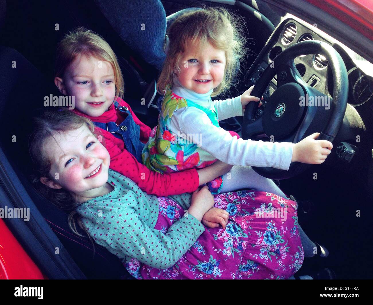 Le giovani ragazze, le tre sorelle, fingendo di guidare un Alfa Romeo auto. Foto Stock