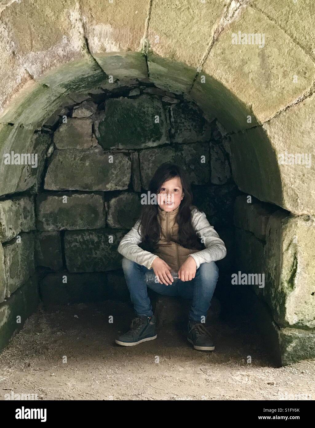 Una giovane ragazza si trova all interno di un antico arco in pietra, guardando nella telecamera. Foto Stock