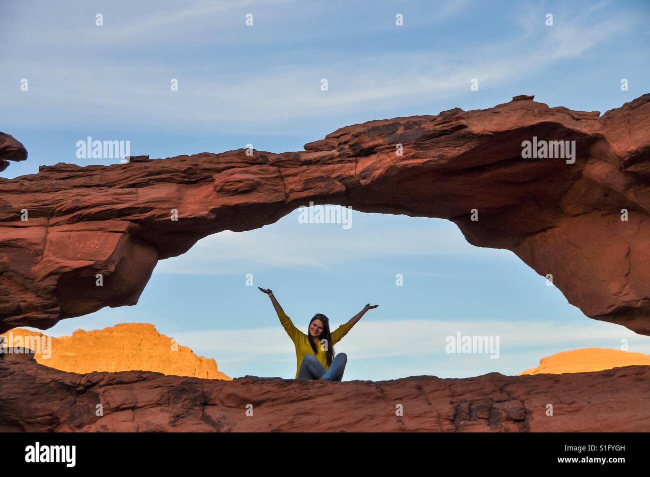 Una ragazza seduta sulla cima della scogliera con le mani in alto Foto Stock
