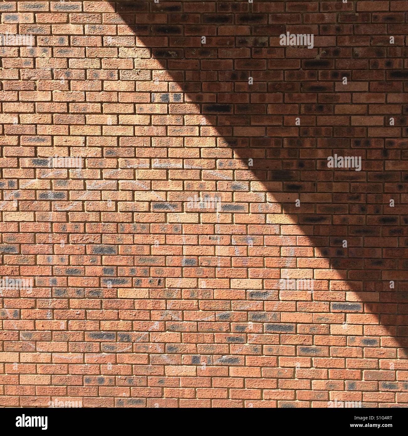 Una diagonale di ombra si divide in rosso di un muro di mattoni in due - Immagine stock catturata con smartphone