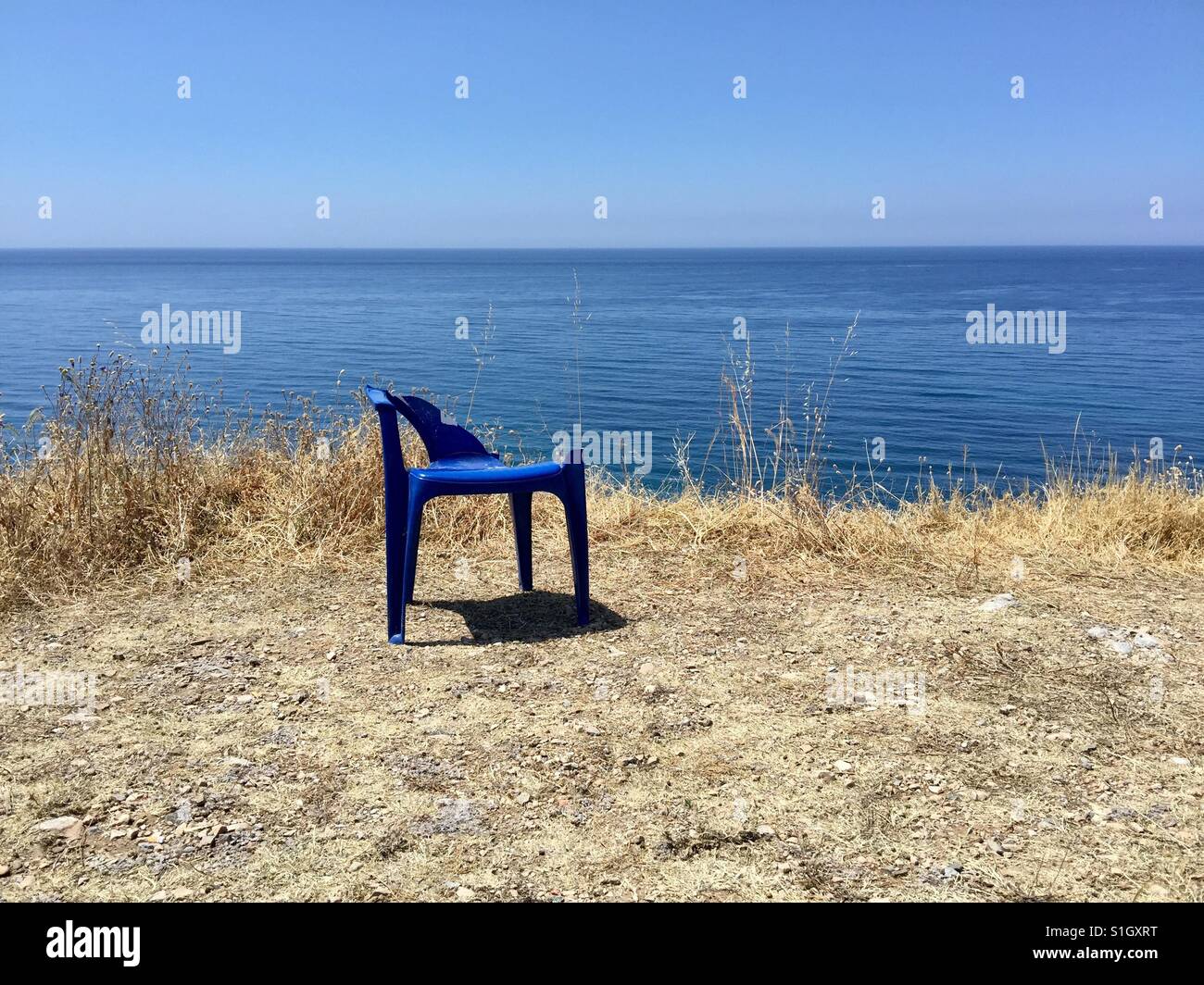 La rottura di una sedia blu abbandonato su uno spagnolo in cima alla scogliera. Foto Stock