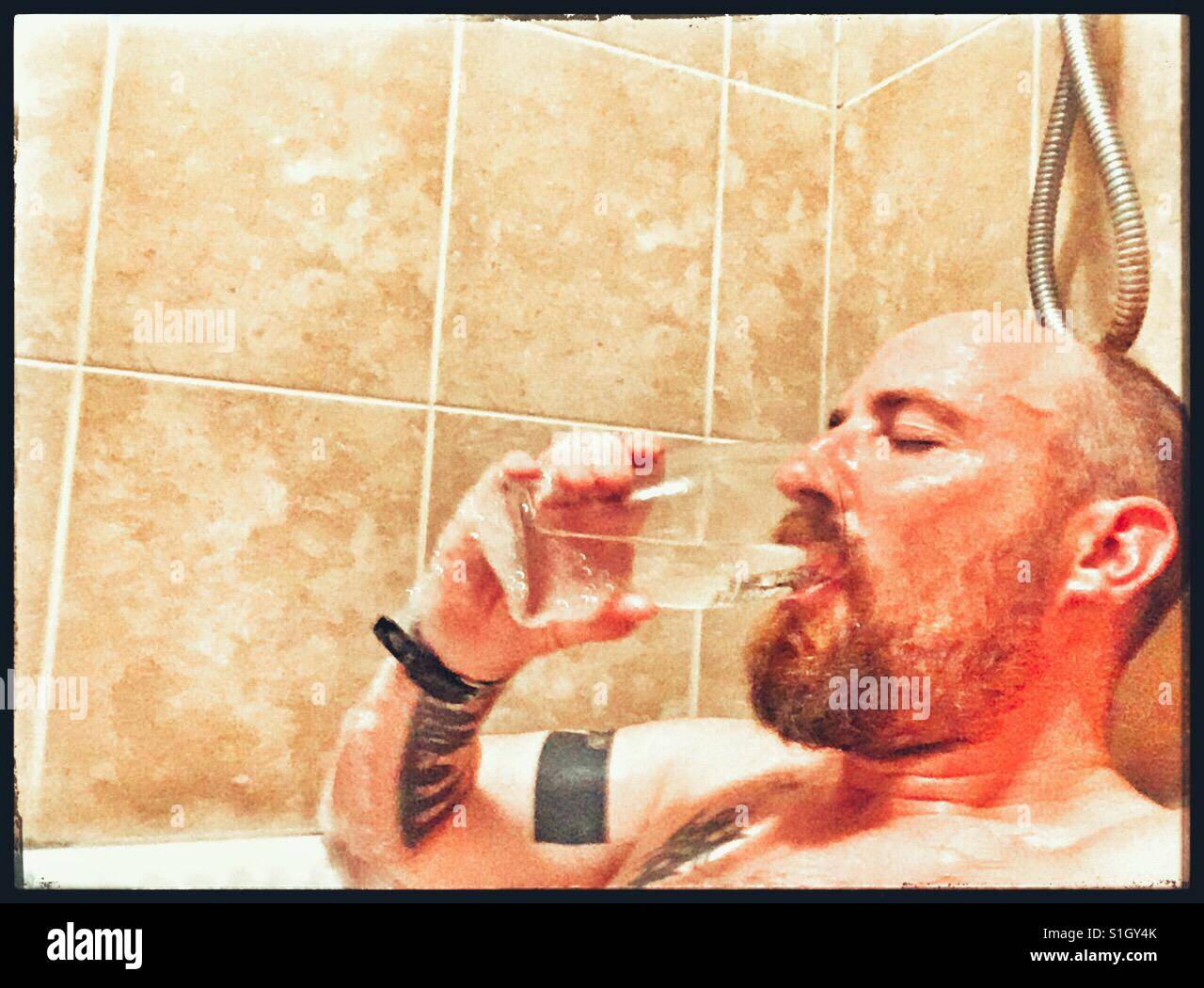 Uomo di bere una pinta di acqua mentre si è immersi in un bagno caldo. Foto Stock