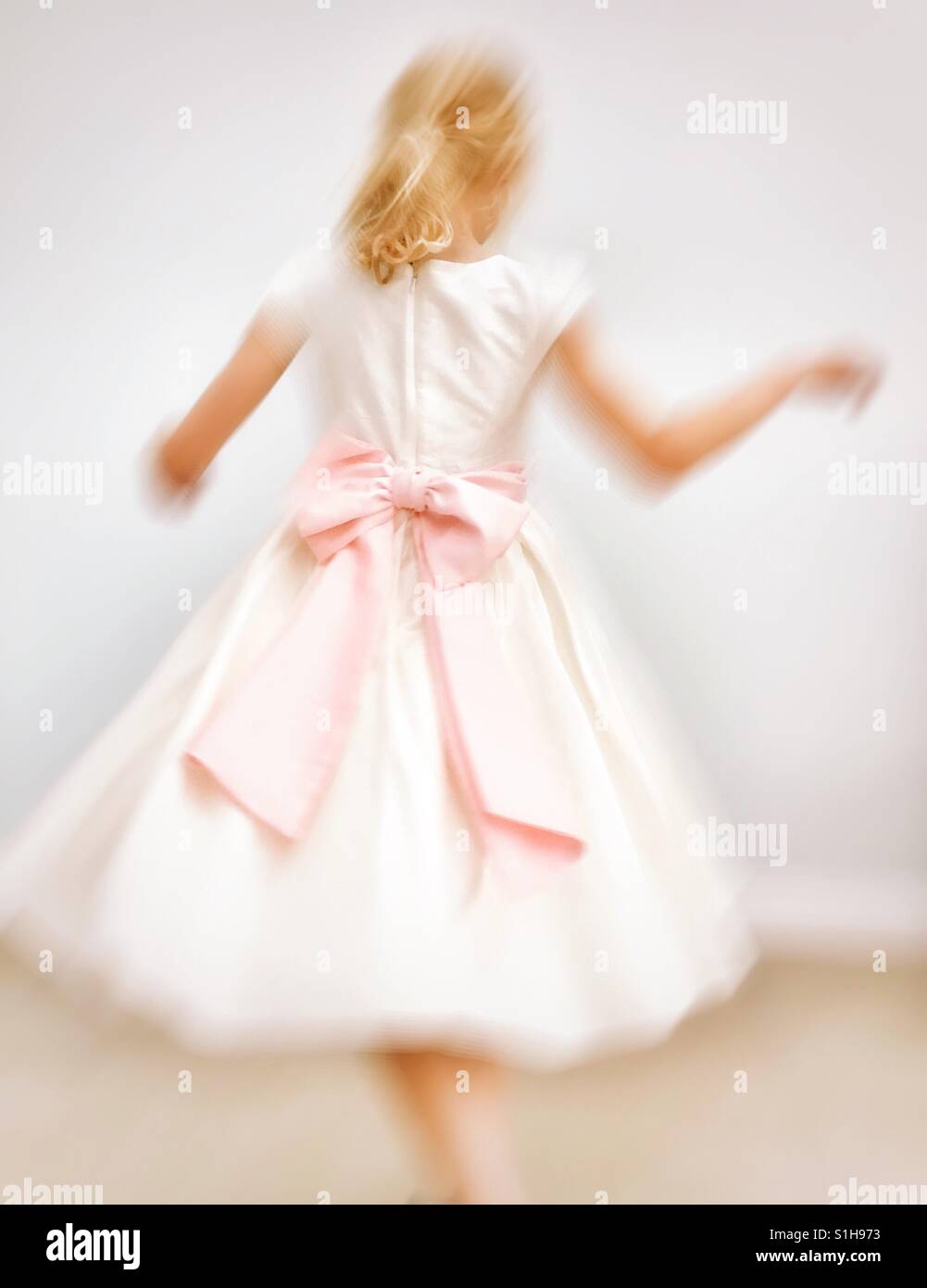 Giovane ragazza in damigelle abito con fiocco rosa fa roteare round Foto Stock