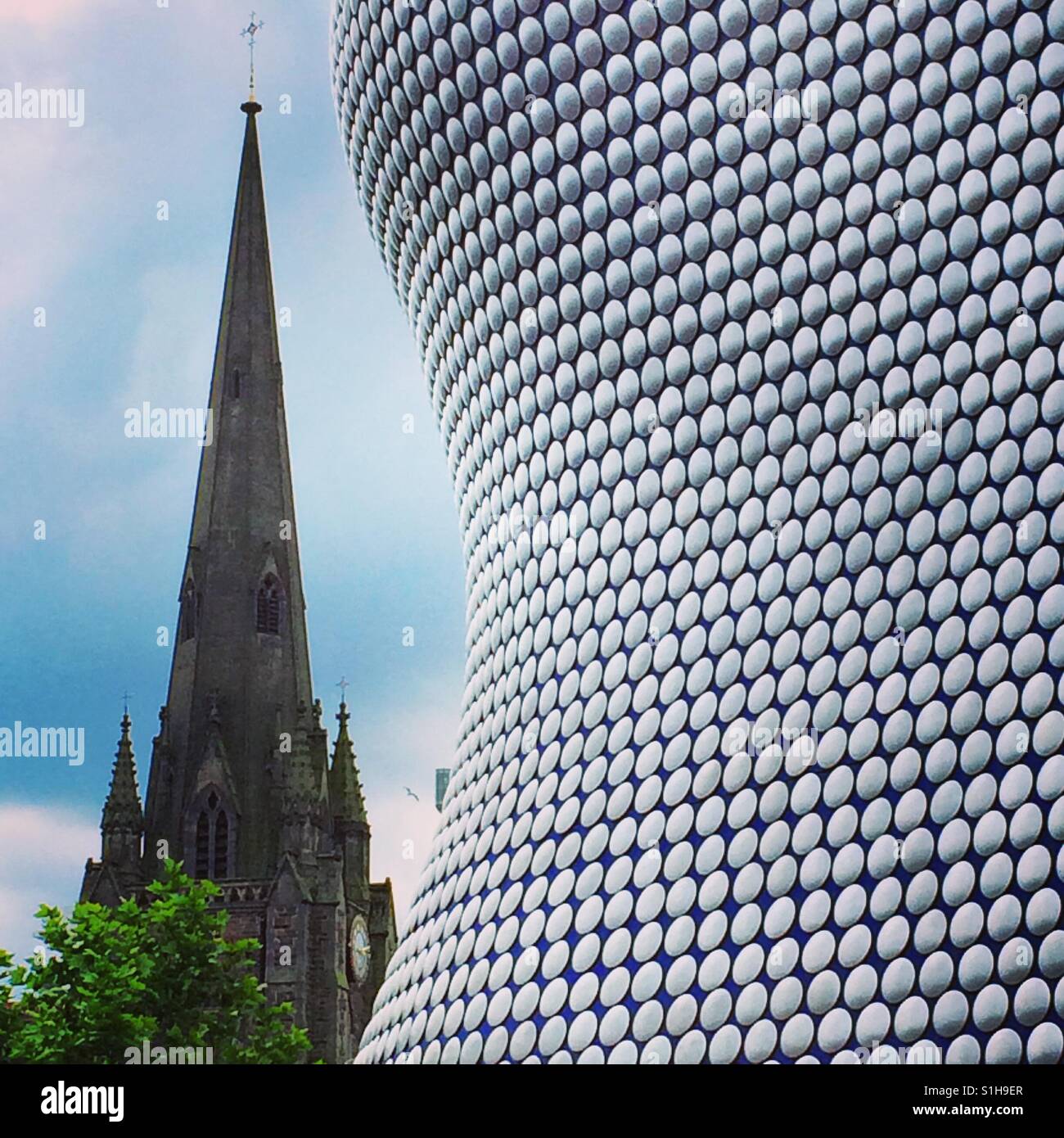 Il design moderno dell'edificio Selfridges a Birmingham, Regno Unito contrasta contro la guglia di una chiesa adiacente Foto Stock
