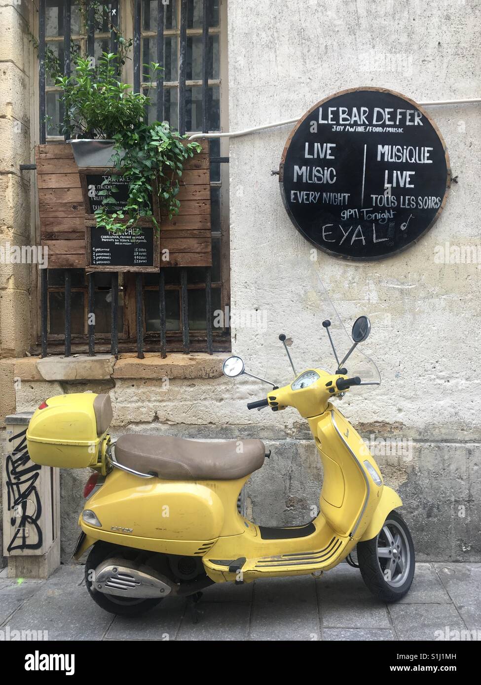 Un giallo brillante ciclomotore parcheggiato di fronte a Parigi cafe finestra con un impianto casella e firmare Foto Stock