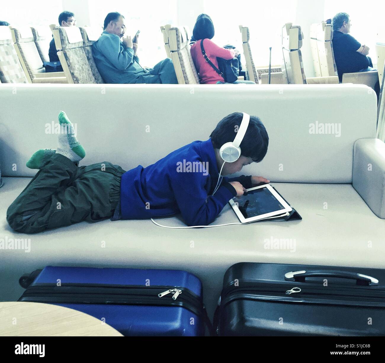 6 anni vecchio ragazzo giocando sulla tavoletta che indossano le cuffie posa su un soft bench di nave giapponese Foto Stock