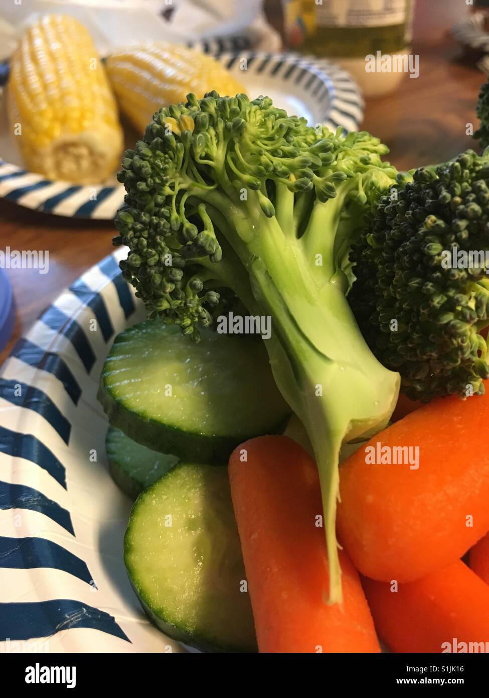 Broccoli, baby carote e cetrioli su un piatto di carta; sulla pannocchia di mais può essere visto in background. - Immagine stock catturata con smartphone