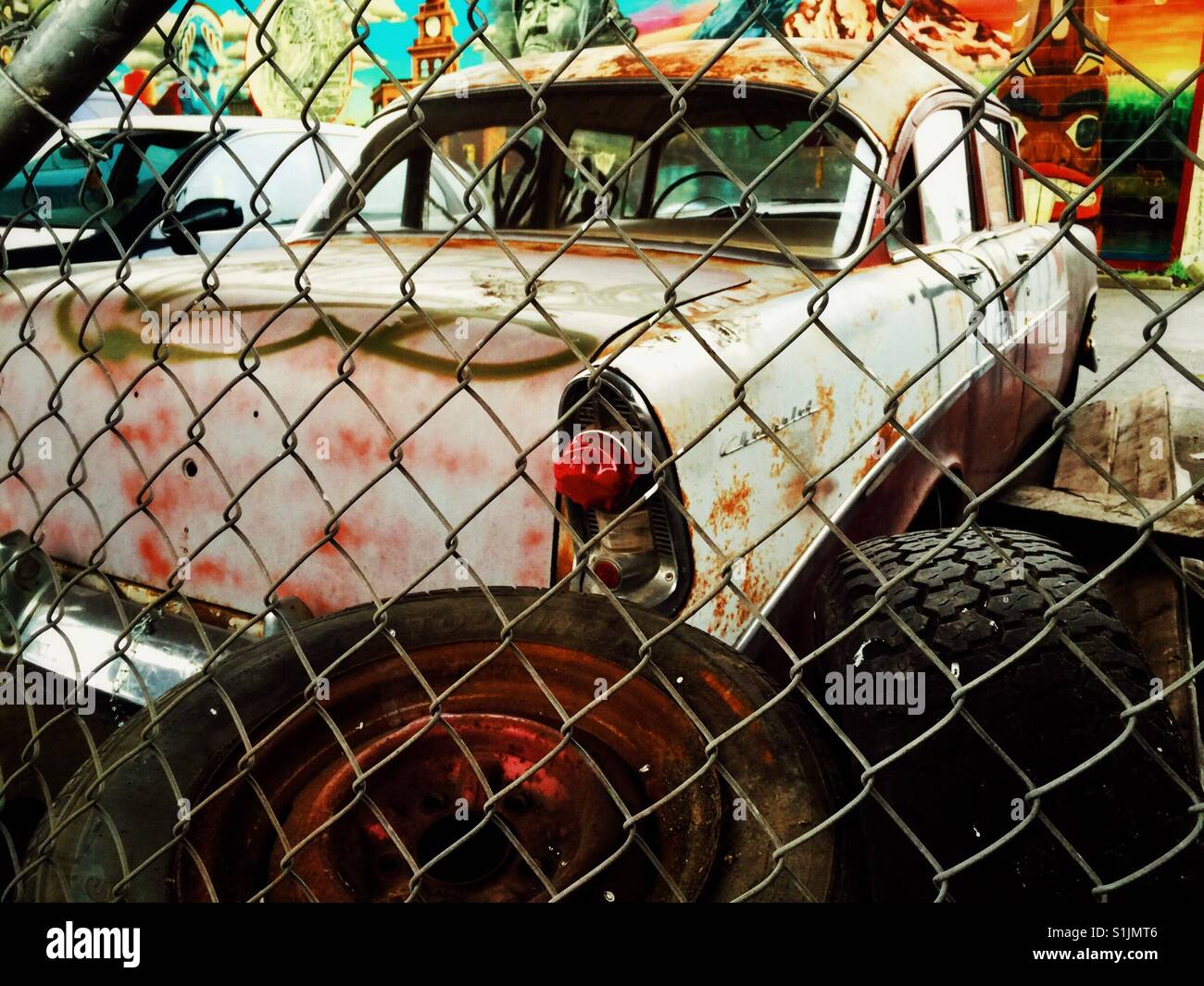 Vintage Chevrolet sedan a sinistra per la ruggine dietro il recinto ad anelli in junk yard in Seattle - Immagine stock catturata con smartphone