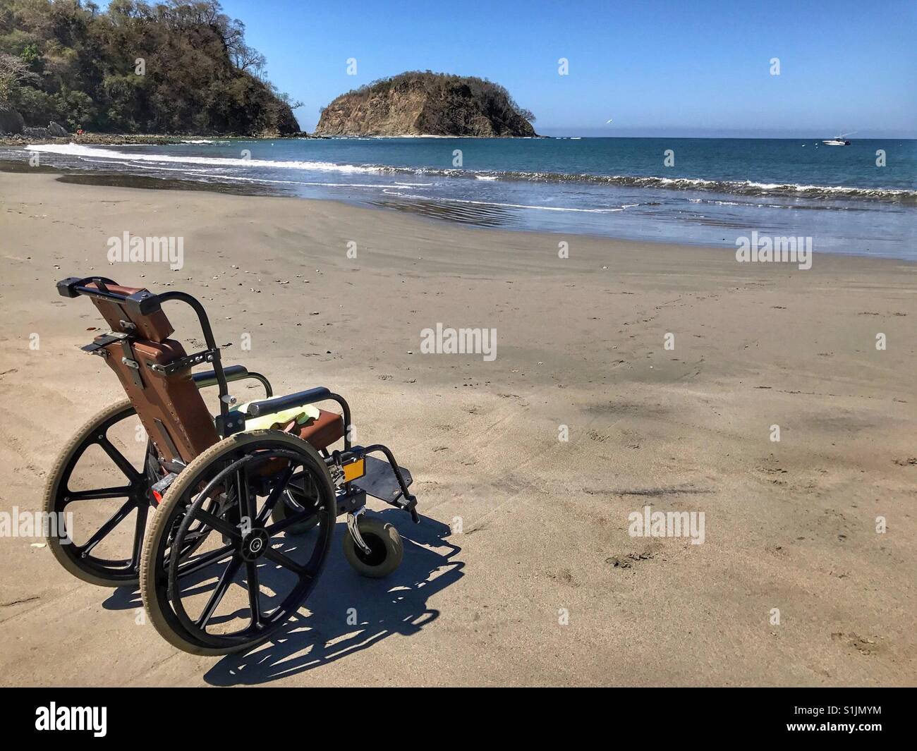Un vuoto che la sedia a rotelle si affaccia sull'oceano dalla spiaggia. Foto Stock
