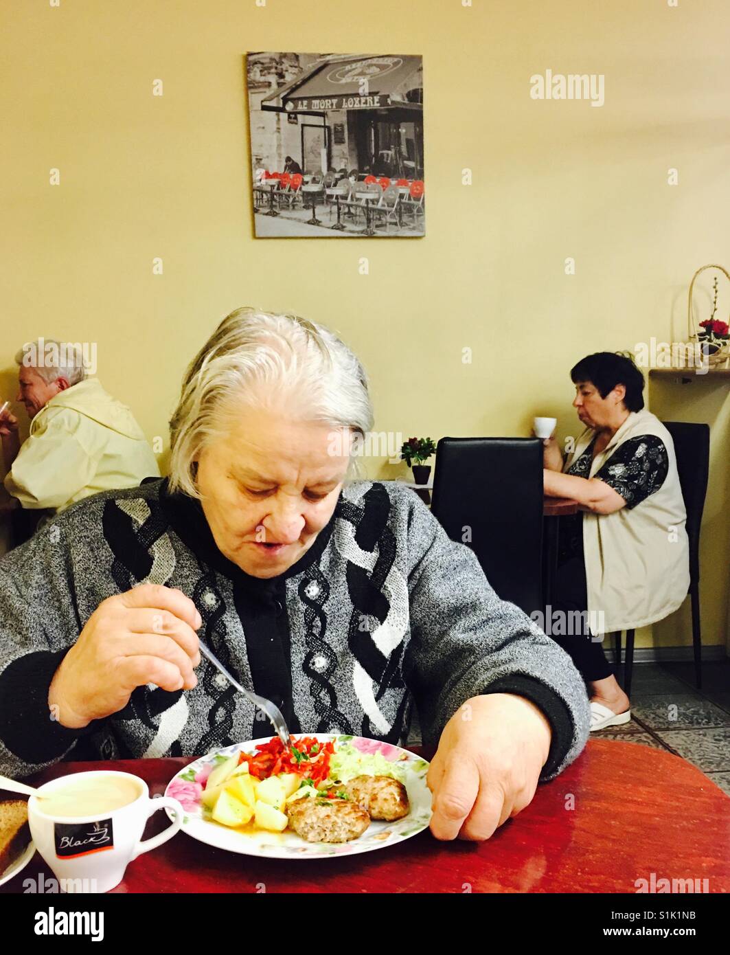 Un'anziana donna lettone di mangiare un pranzo tradizionale in una piccola caffetteria presso il mercato centrale di Riga. Foto Stock