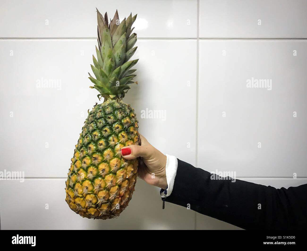 Donna che mantiene un ananas contro un bianco parete piastrellata - Immagine stock catturata con smartphone