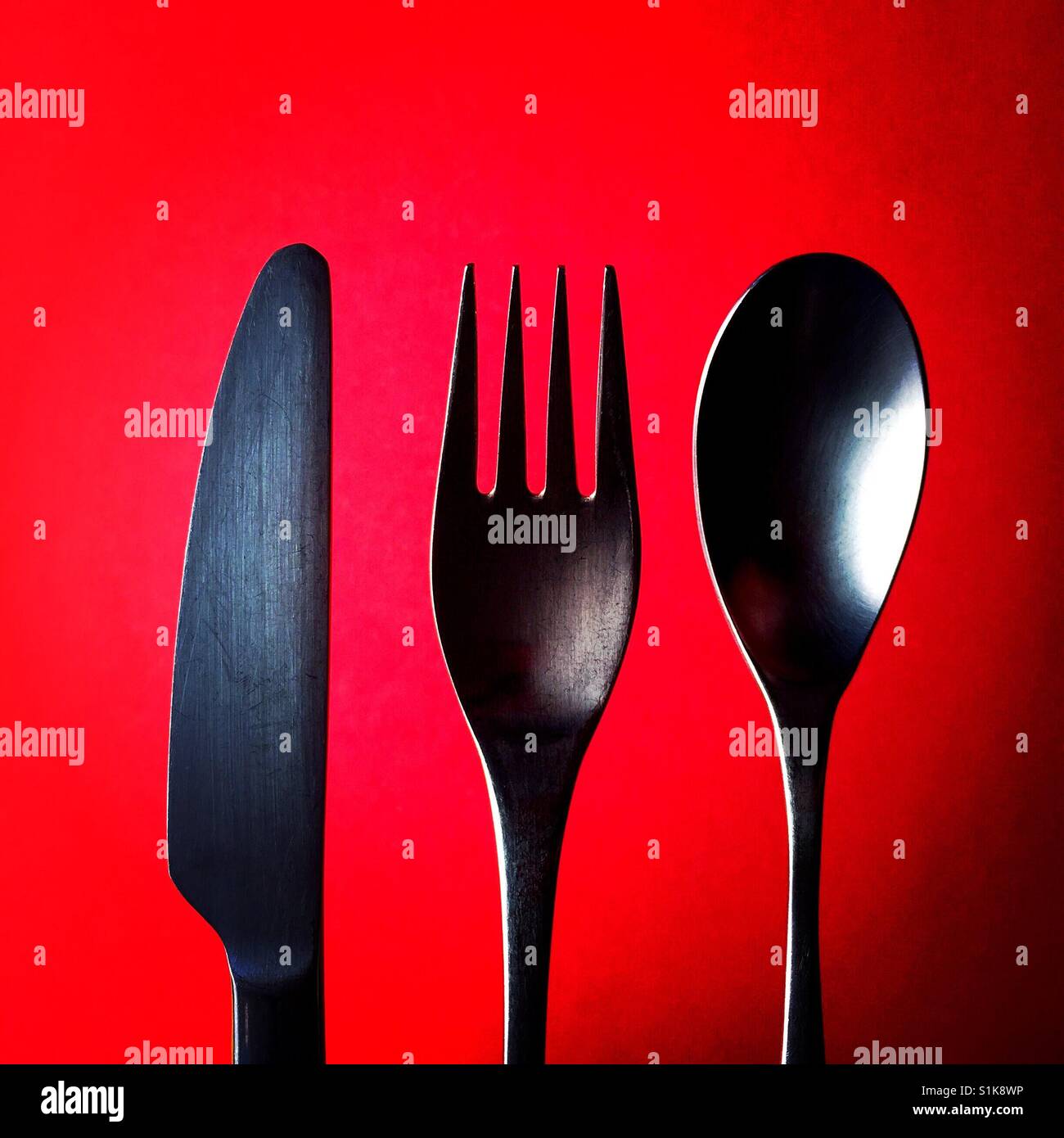 Una chiusura tettuccio di colpo di un coltello e una forchetta e un cucchiaio sopra uno sfondo rosso Foto Stock