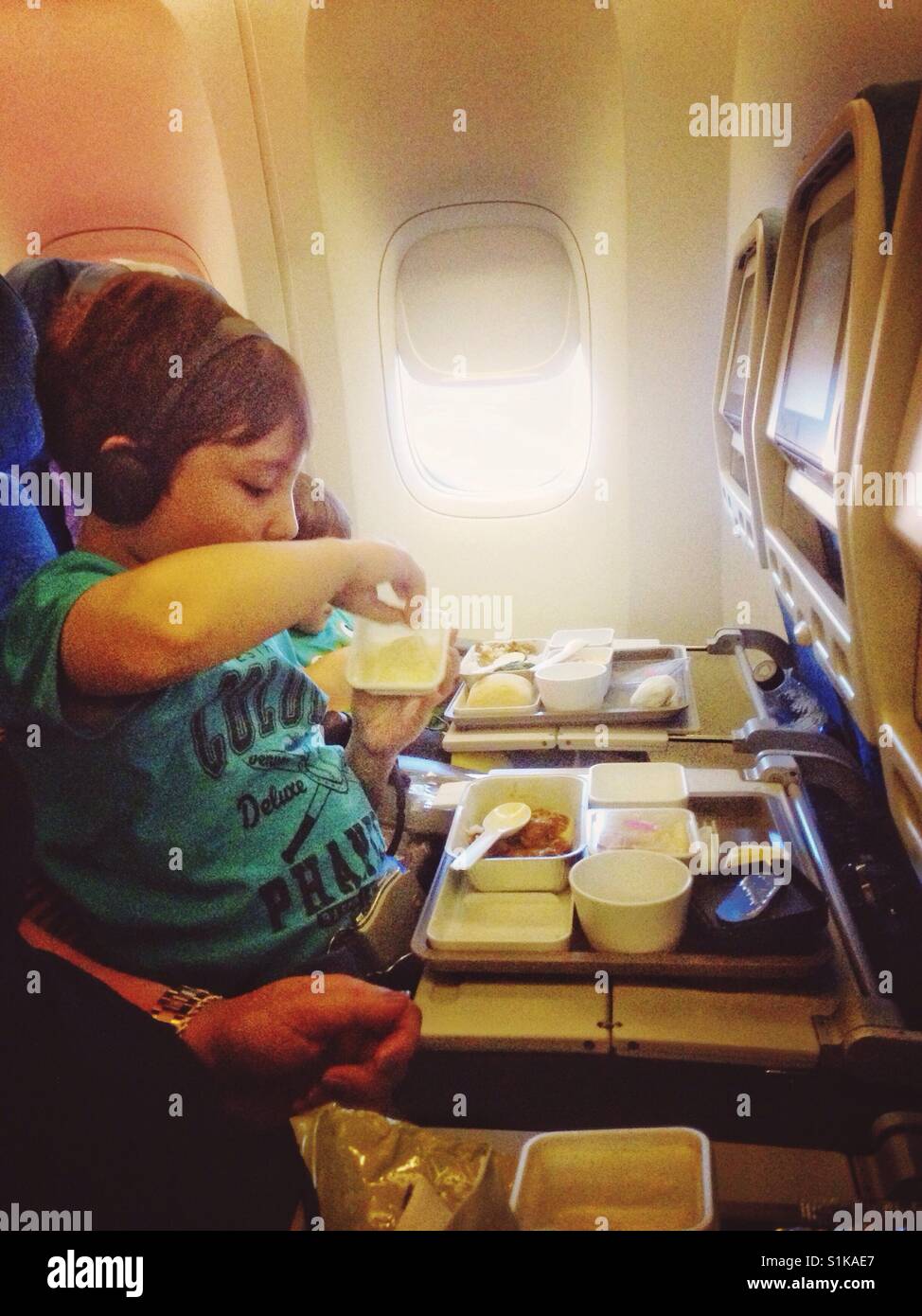 Un ragazzo gode di un pasto a bordo di un voli di lungo raggio. Foto Stock