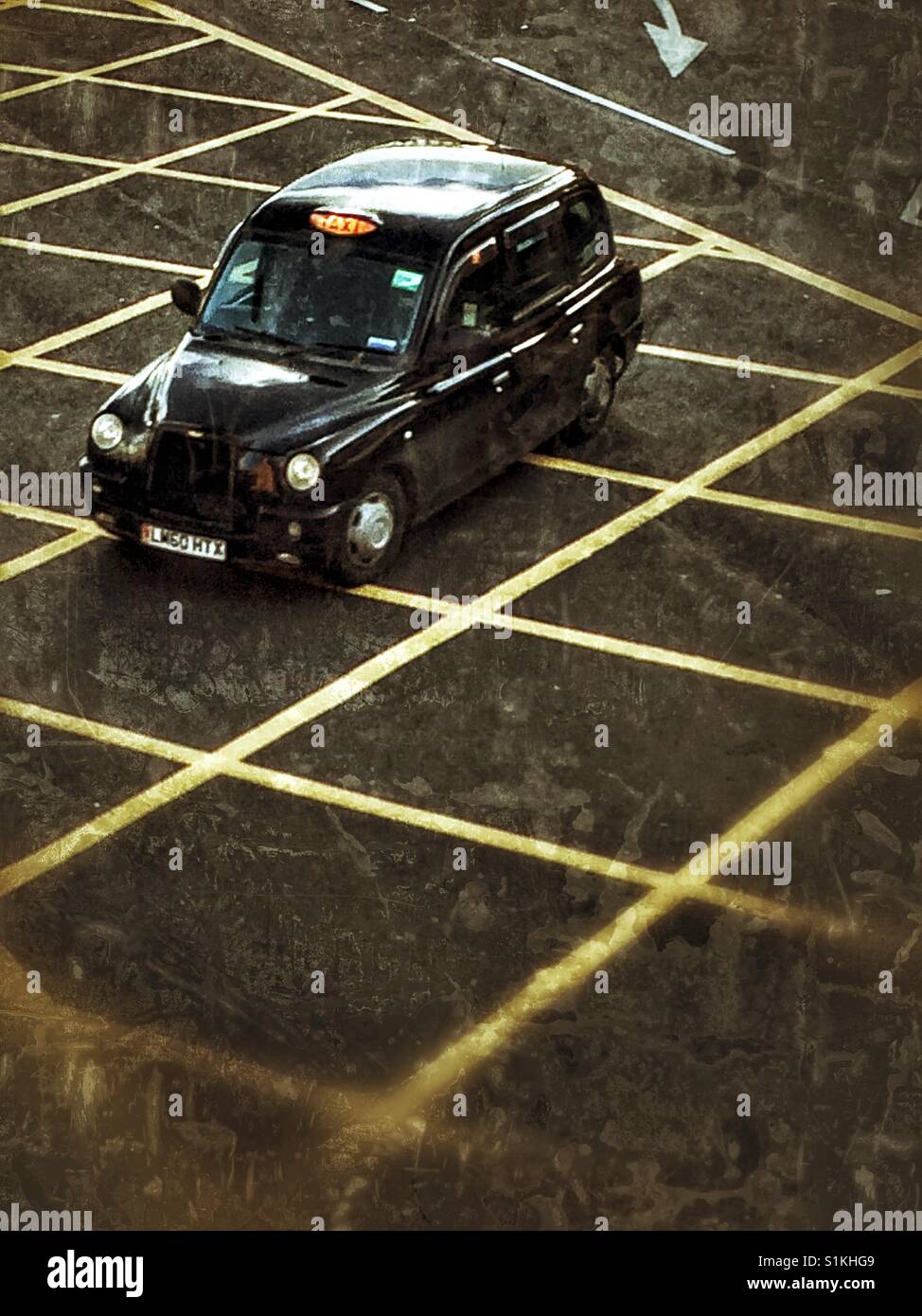 Guardando verso il basso a partire da sopra su un Black Cab di Londra o taxi accelerando su pericolo giallo linee su una strada di Londra. Foto Stock