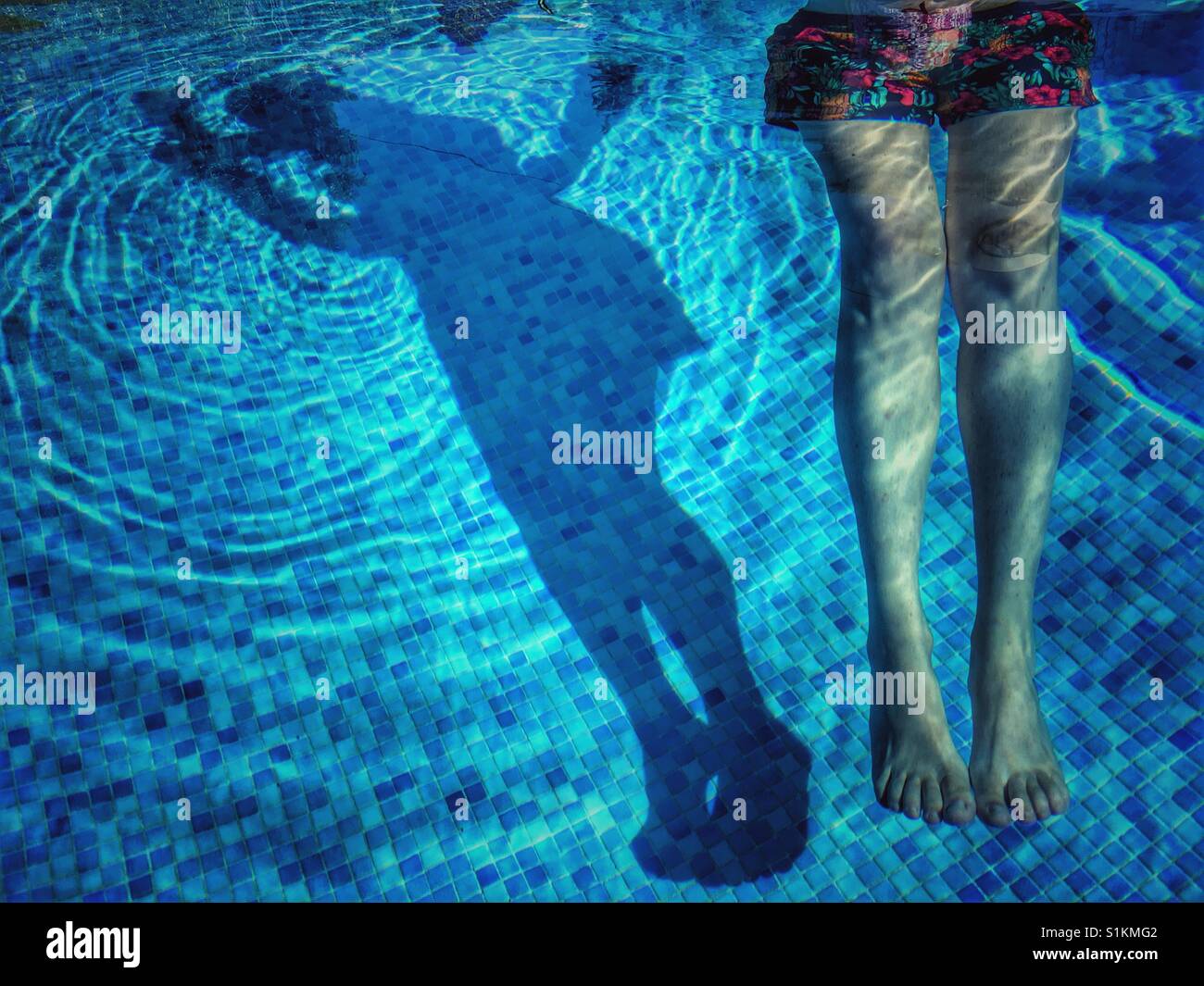 Donna galleggianti in piscina usando un pool noodle e la sua ombra sul fondo ricoperto di mattonelle della piscina. Foto Stock