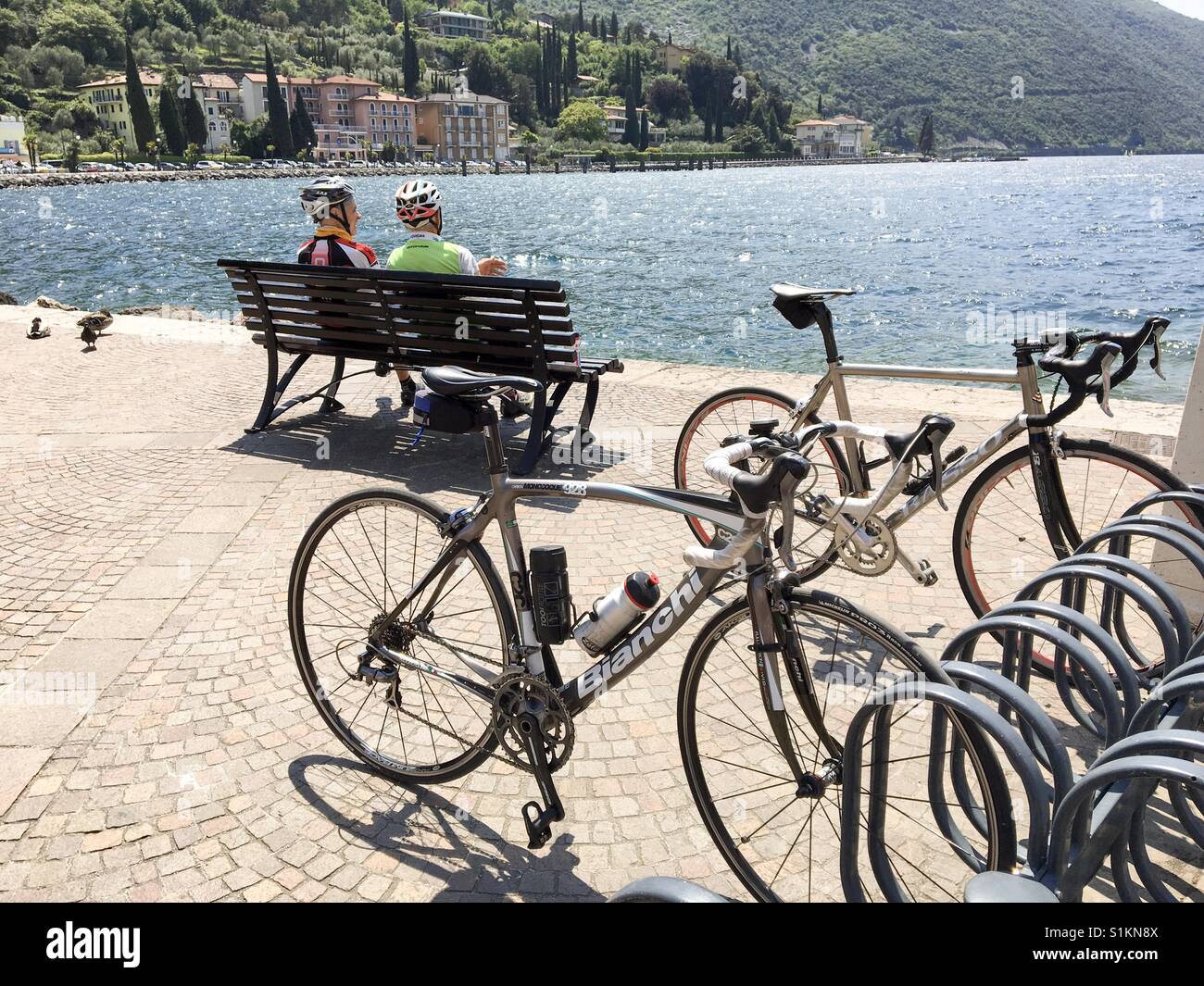 A Torbole sul lago di Garda, Italia- Maggio 2017: Due ciclisti prendere un meritato riposo dal loro viaggio lasciando le loro biciclette in rack fornito sul lungomare Foto Stock
