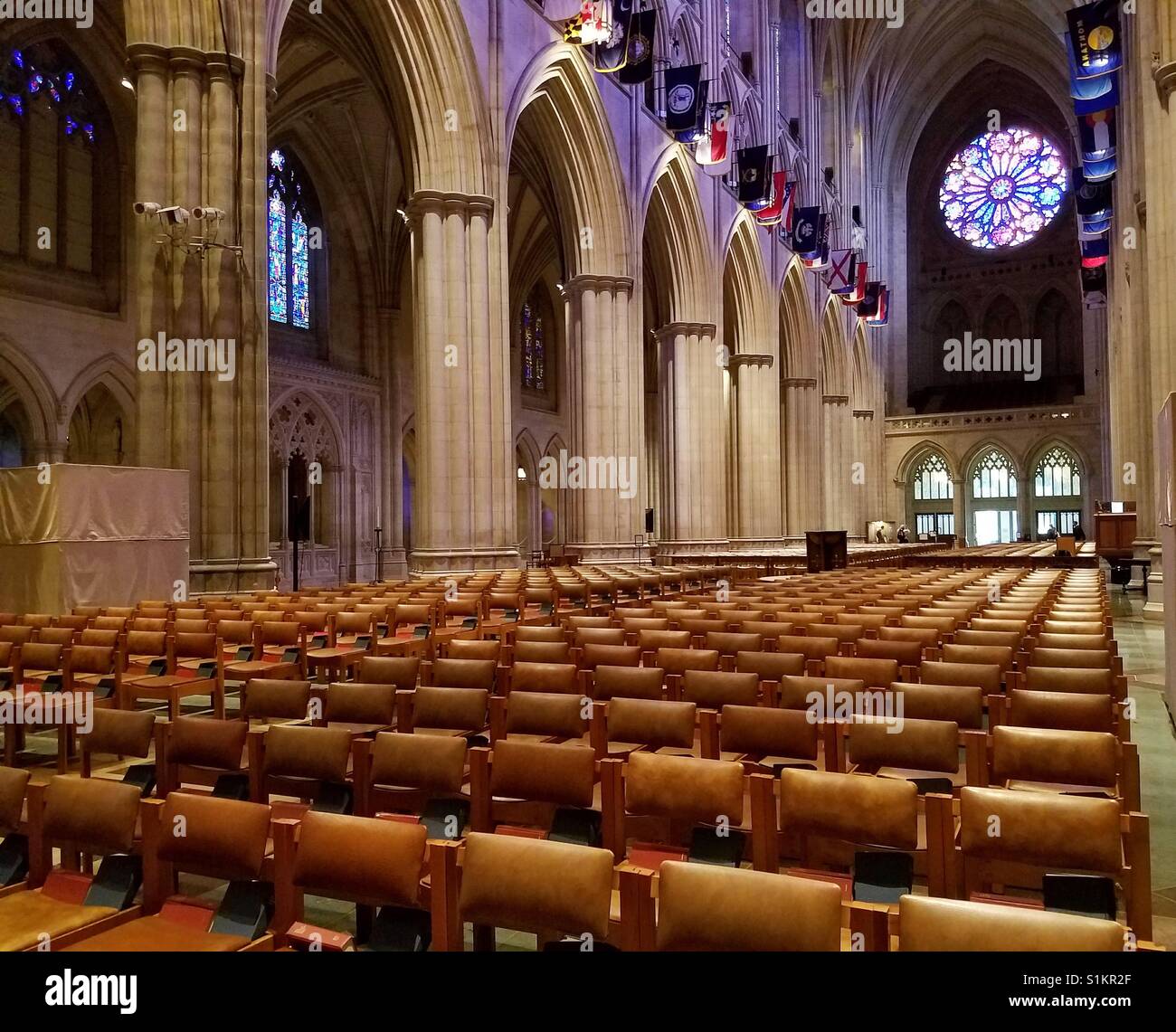 La Cattedrale Nazionale di Washington interno. Vista del famoso West rosone con il sole che splende attraverso. Cattedrale gotica con archi fodera la navata e inquadrare le sedie removibili. Foto Stock