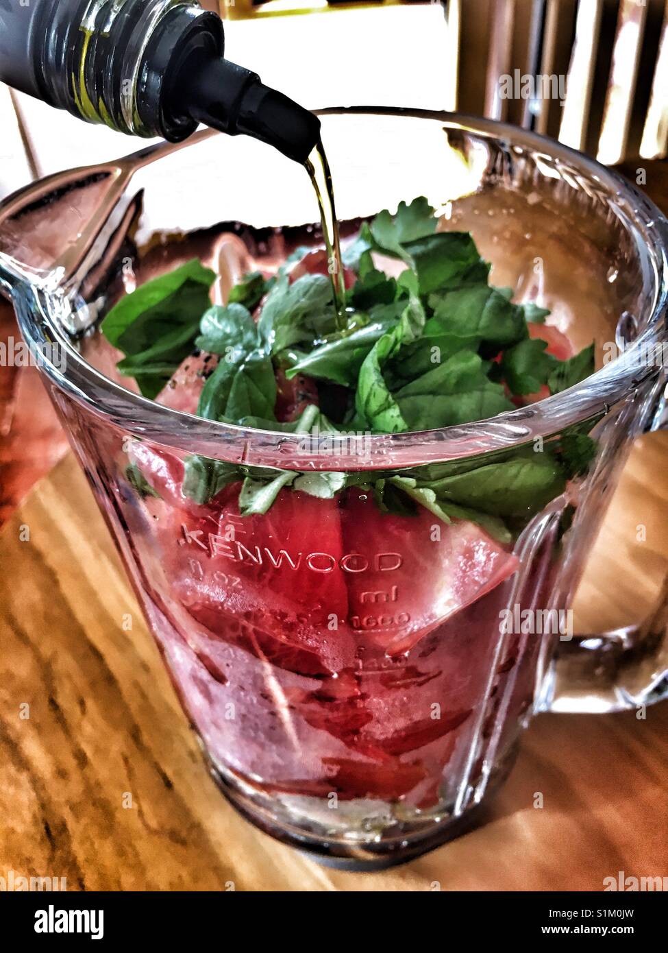Aggiunta di olio di oliva per gli ingredienti per il gazpacho in un vetro Kenwood frullatore caraffa. - Immagine stock catturata con smartphone